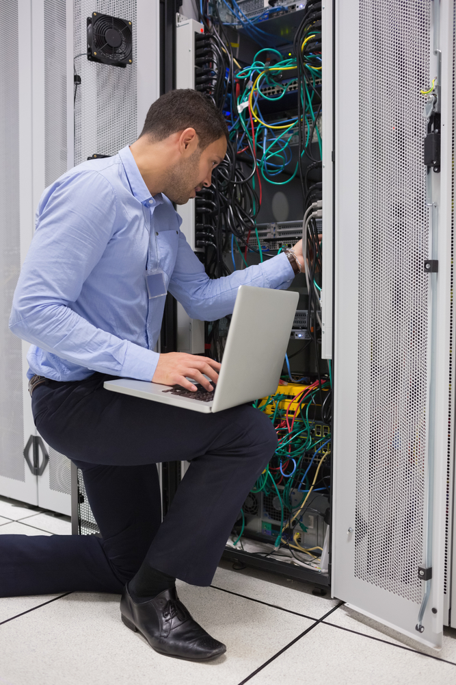 Man fixing wires while doing maintenance with laptop in data center